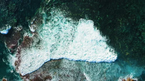 Aerial top down view of waves crashing on coastal rocks and making white foam Video stock 227010364