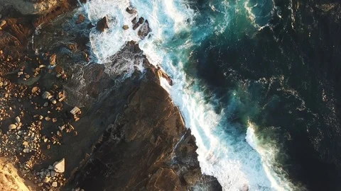 Aerial top down of waves breaking on cliff side rocks Stock Footage 88672749