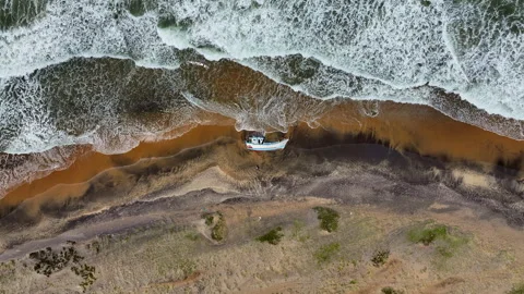 Aerial Top Lockdown Shot Of Nautical Vessel Fallen On Beach By Waves In Sea - Stock Footage 260346359