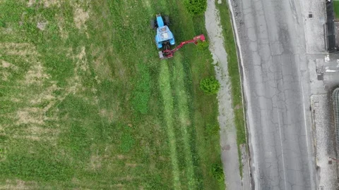 Aerial top view of blue tractor mowing grass near roadside with precision Video stock 315280067