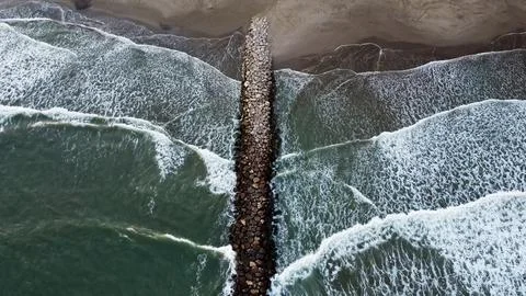Aerial Top View Drone Footage Of Ocean Waves Reaching Shore stone breakwater Stock Photos