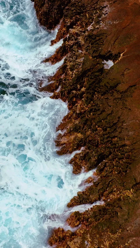 Aerial top view of large ocean waves with spray crashing against the rocky cliff Stock Footage 307037844