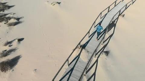 Aerial top view of a man running in a wooden boardwalk at the desert sand beach Stock Footage 146186953