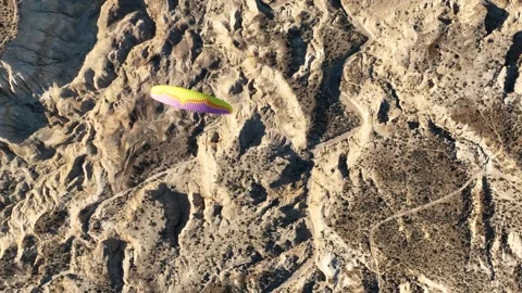 Aerial top view of multi colored paragliding flying over desert badlands area Stock Footage 285145920