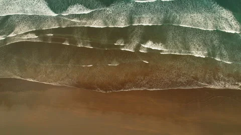 Aerial top view of ocean waves forming white foam patterns on dark sandy beach Stock Footage 345536968