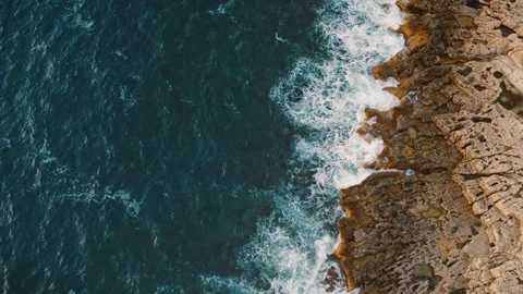 Aerial top view of sea waves foaming over sharp jagged coastal rocks Stock Footage 345536520