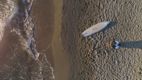 Aerial top view of young man surfer wearing wetsuit sitting with surf board Stock Footage 85117575