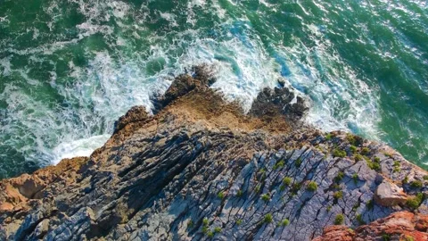 Aerial topdown linear shot of waves hitting a rocky cliff by green ocean water Stock Footage 165461726