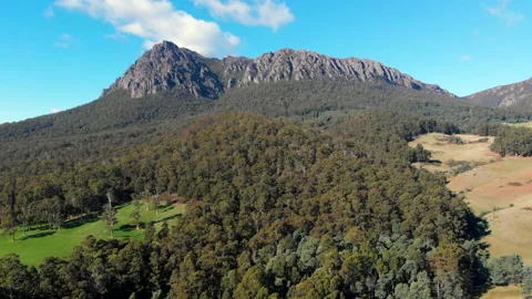 Aerial tracking mountain peak surrounded by forest and scattered pastures Stock Footage 154489113