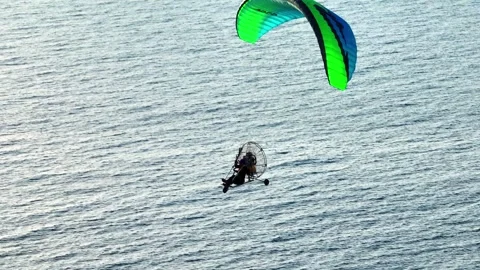 Aerial tracking of a paramotor flying over the sea with a drone Stock Footage 266389720