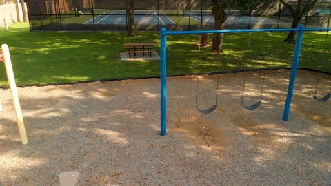 Aerial tracking right past empty swings of a playground Stock Footage 115954277