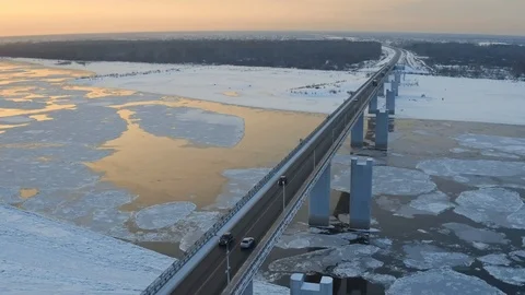 Aerial tracking shot alone car crossing bridge over winter river with ice floes Stock Footage 99911751