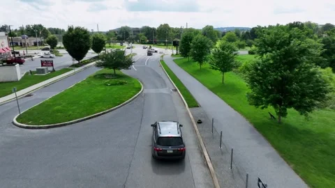 Aerial tracking shot of Black suv car on road in green city during sunny day Stock Footage 315434609