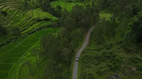 Aerial tracking shot of a car driving down the mountain road, small village in Stock-Footage 249403045