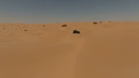 Aerial tracking shot of a Range Rover Classic navigating deep sand dunes in the 動画素材 335445358