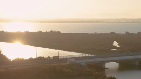 Aerial tracking shot of small car driving beside ocean crossing bridge at dusk Stock Footage 112716150