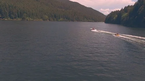 Aerial tracking shot of speedboat pulling woman on inner tube across lake Stock Footage 84186270