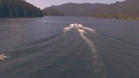 Aerial tracking shot of speedboat pulling woman on inner tube across lake Stock Footage 84186498