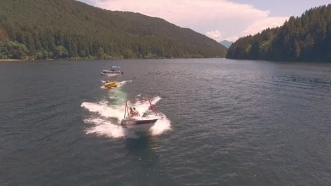 Aerial tracking shot of speedboat pulling women and kid on inner tube on lake Stock Footage 84250392