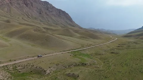 Aerial tracking shot of an SUV on a dirt road in a mountain valley, Kyrgyzstan Видео 347240953