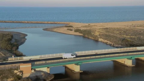 Aerial tracking shot of van driving beside ocean crossing bridge at dusk Stock Footage 112716240