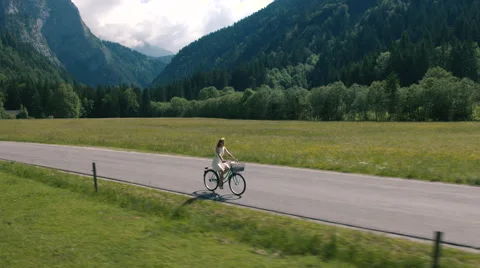 Aerial - Tracking shot of a woman in a white dress riding bicycle on rural road Stock Footage