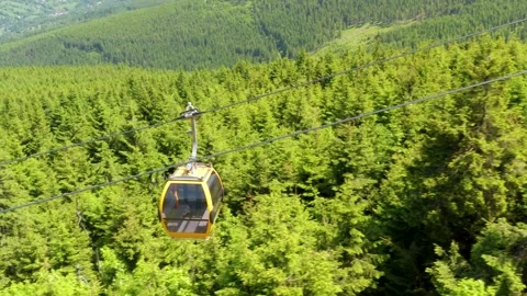 Aerial tracking shot of yellow mountain gondola cabin passing over forest Stock Footage 312593136