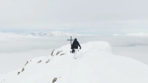 Aerial tracking view of snowboarder standing by a summit cross on a mountai.. Stockbeeldmateriaal 342492116