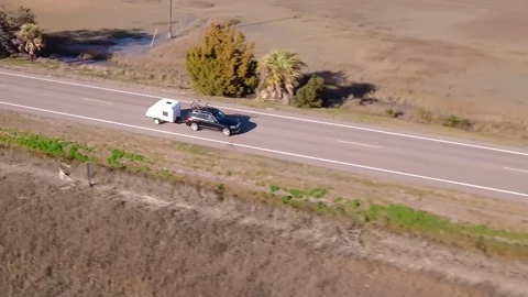 Aerial tracking view of vehicle pulling teardrop camper along coastal highway. Stock Footage 124388527
