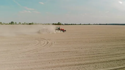 Aerial: tractor processes dusty, poor-yielding farmland with a modern combined Stock Footage 123394479
