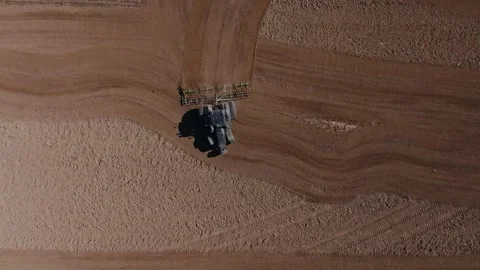 Aerial tractor pulls cultivator across curved freshly tilled farmland Video stock 337583467