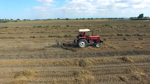 Aerial tractor pulls a rake across a harvested yellow field - Fodder and Grain Stock Footage 339341921