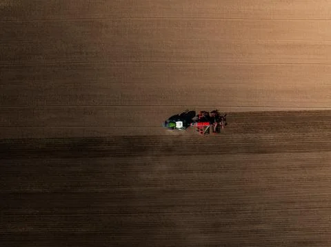 Aerial tractor with red implement plows parallel furrows in field Stock Photos
