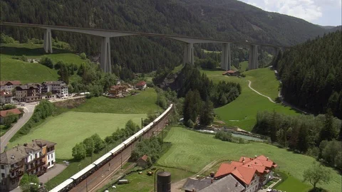 Aerial of train running through mountain forest, Viaduct over valley and village Stock Footage 109153870