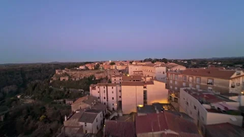 Aerial twilight view of hillside town, glowing streetlights lining narrow Stock Footage 330254631