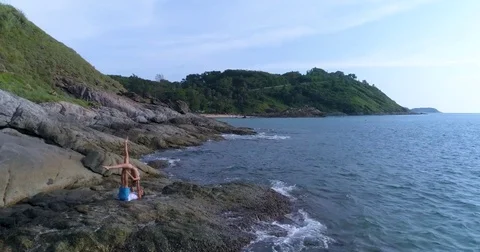 Aerial: Two partners doing Acro Yoga on the rocks. Aerial view on the beach. Stock Footage 82189568