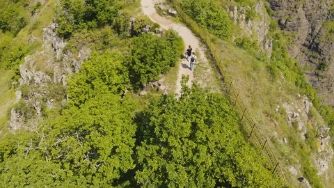 Aerial of two tourists walking on path at top of mountain. Pair goes from 库存影片 92544854