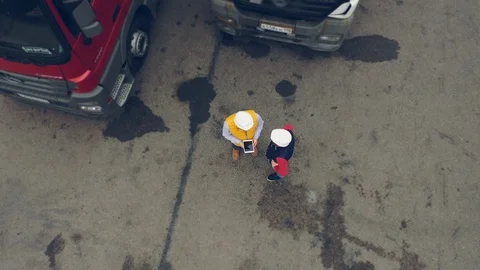 AERIAL. Two workers works on tablet near trucks. Camera zooming out. Stock Footage 111404655