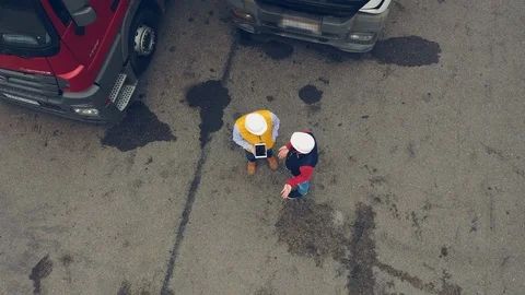 AERIAL. Two workers works on tablet near trucks. Camera zooming out. Stock Footage 111404910