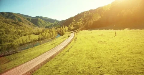 Aerial UHD 4K view. Low air flight over mountain rural dirt road and meadow at Stock Footage