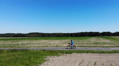 AERIAL: Unrecognizable man speeds down a single trail crossing a large meadow on Stock Footage 132049528