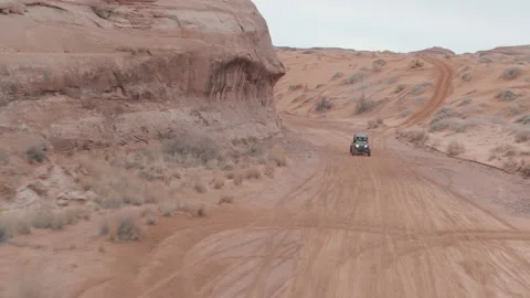 Aerial of UTV driving through red and pink sand wash in Utah desert landscape Stock Footage 233842106