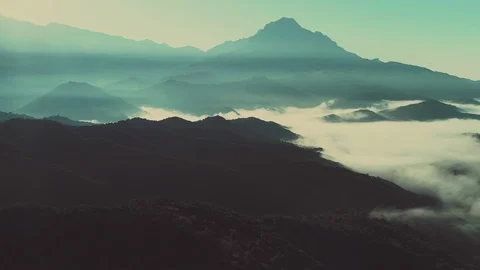 Aerial valley below clouds amongst mountains at sunrise Stock Footage 89814309