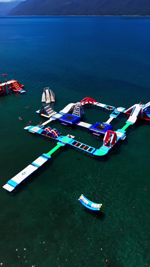 Aerial vertical panning shot of a large inflatable water park on a clear bl.. Video stock 339252216