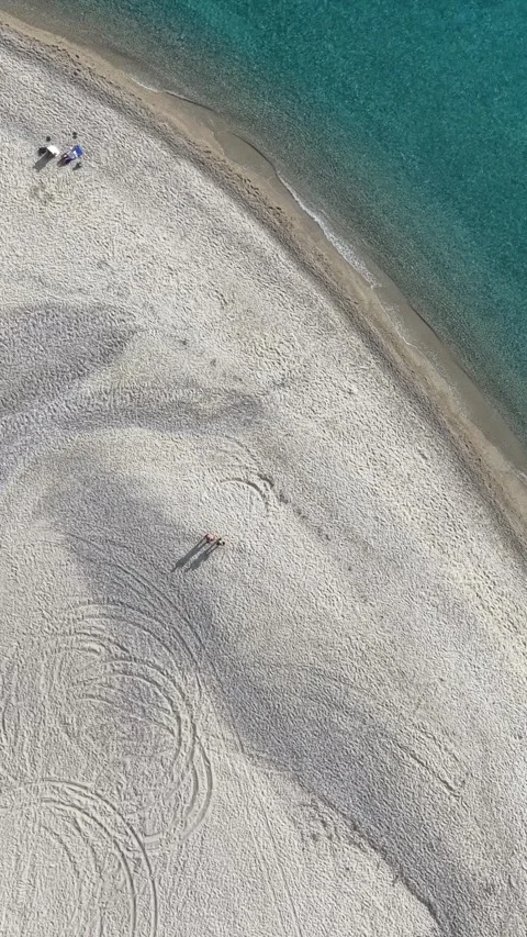 Aerial vertical top down view of a couple sunbathing on sandy beach with long sh Stock Footage 341461012