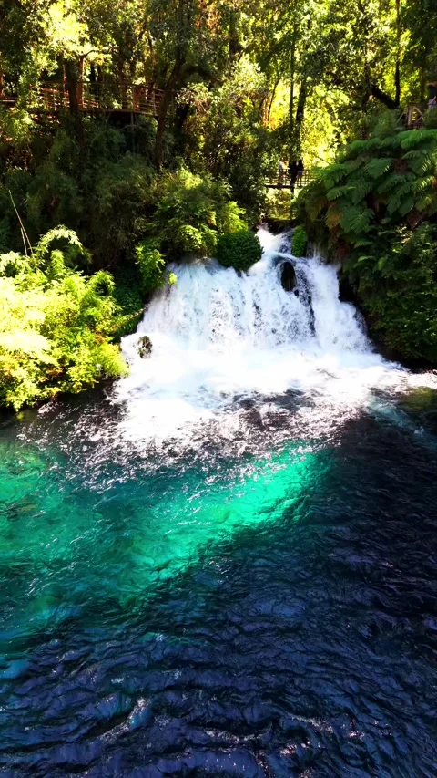 Aerial vertical tracking shot panning over a roaring waterfall flowing into.. Video stock 339252193