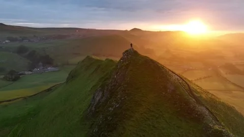Aerial video of a man standing on a mountain and looking at the landscape at Stock Footage 242529560