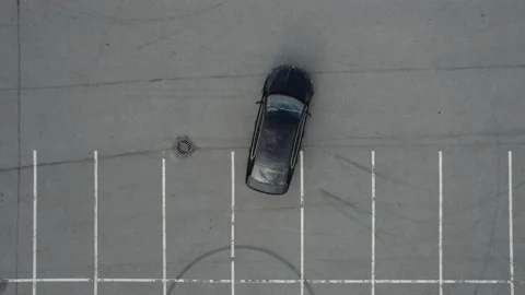 Aerial viev a black car in an empty parking lot leaves the parking slot on a sun Stock Footage