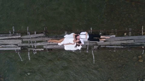 Aerial view. 4k. Fly over the couple lying on the bridge over a mountain river. Stock Footage 101792040