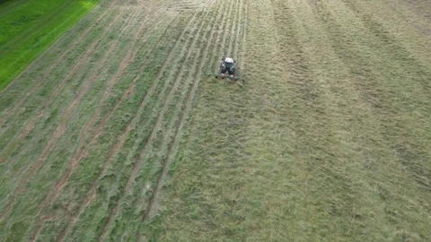 Aerial view from above and behind tractor with tedder attached working in field Stock Footage 276962529